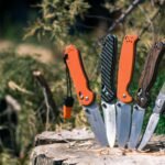 A collection of stylish pocket knives displayed outdoors on a tree stump.