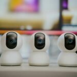 Three modern smart home security cameras placed on a table indoors with a blurry background.