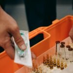 Close-up of hands organizing vials and syringe in a medical first aid kit, emphasizing emergency readiness.