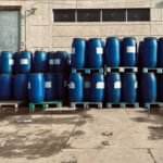 Rows of blue industrial barrels stacked on pallets outside a warehouse.