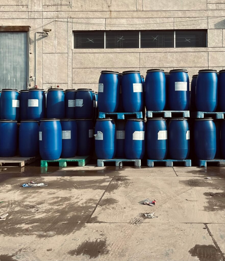 Rows of blue industrial barrels stacked on pallets outside a warehouse.