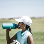 Woman golfer taking a break to hydrate on a sunny day in a field.